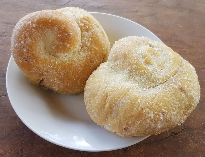 Two sugar-topped ensaymada pastries on a white plate