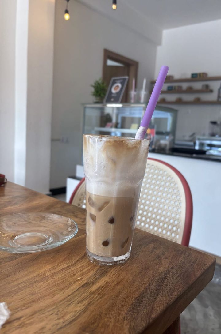 Iced latte in a tall glass with a purple straw on a wooden table