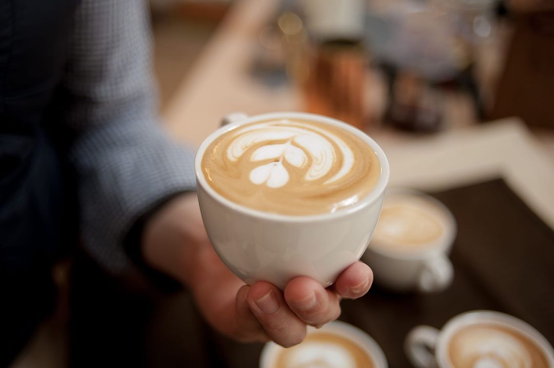 A hand holding a cup of latte with a heart pattern in the milk foam